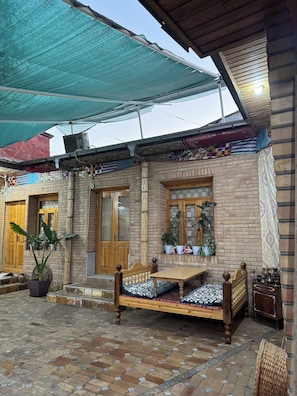 A traditional house with a tiled patio, a wooden bed, and a large shaded area.