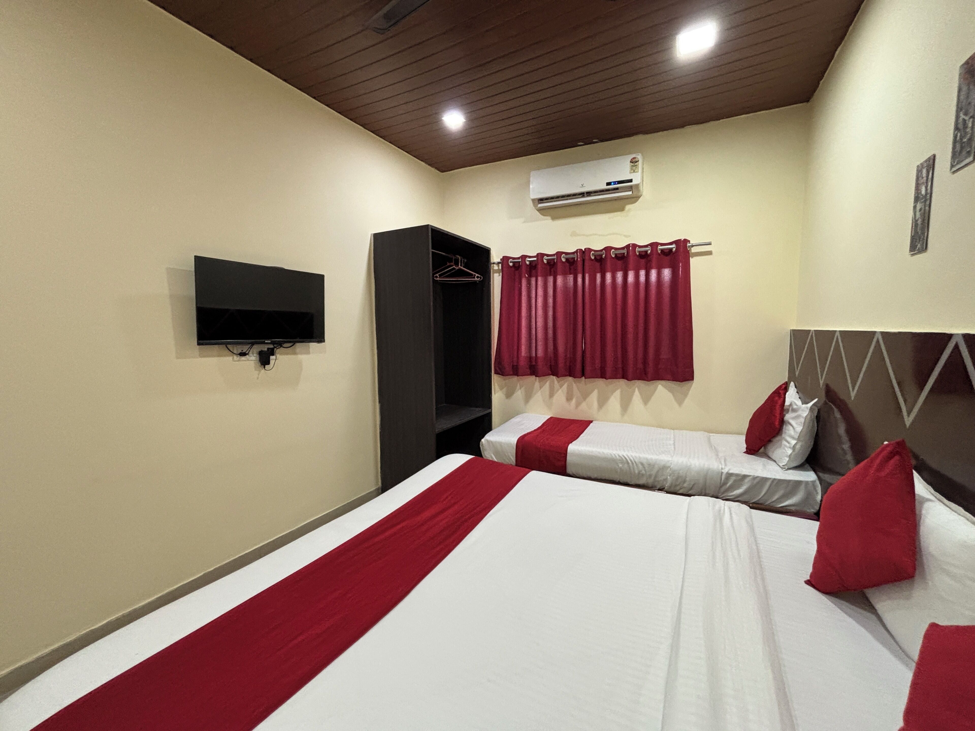 A hotel room with two beds, a TV, an air conditioner, and a wardrobe.