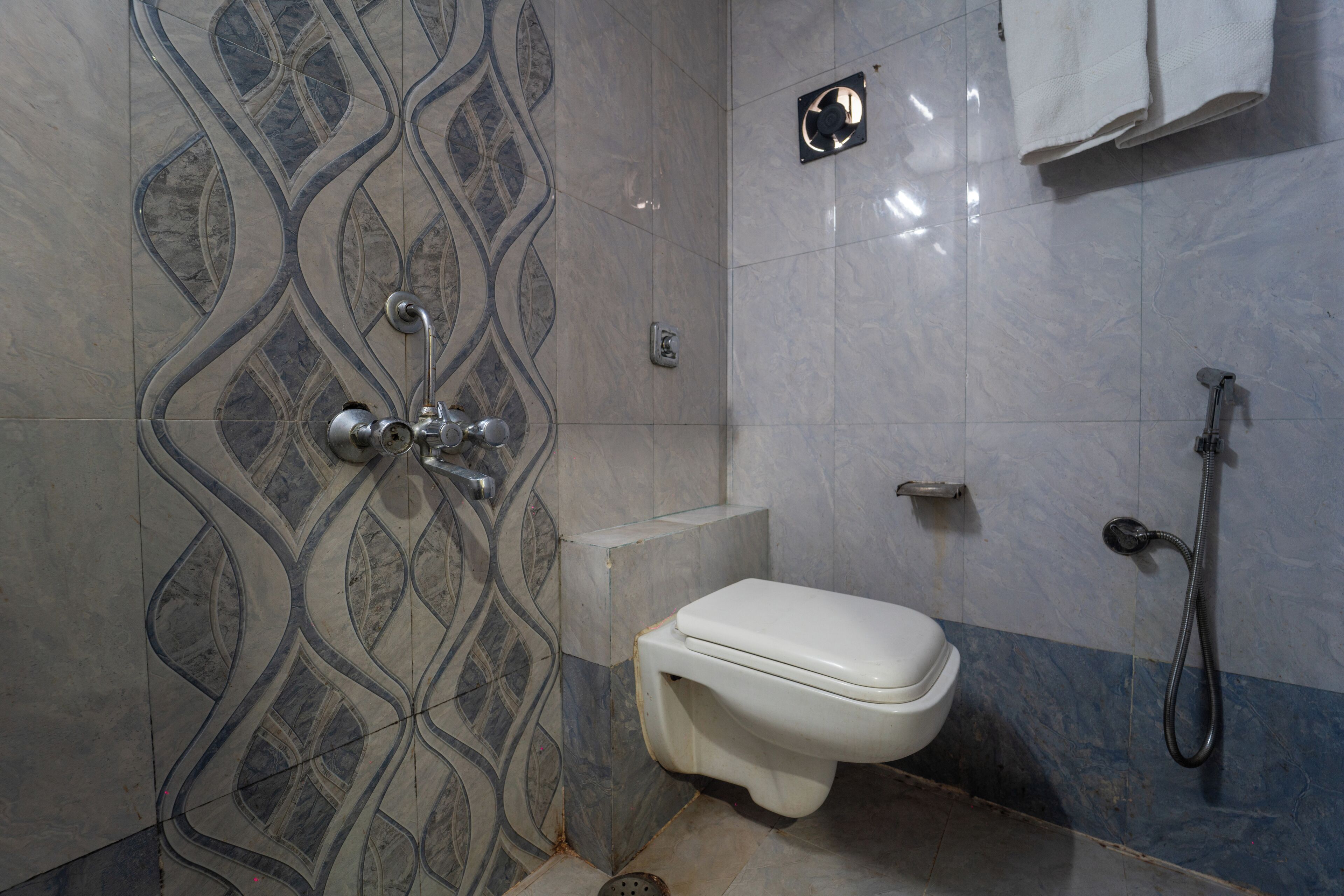 A bathroom with a patterned tile wall, a toilet, a shower, and a towel rack.