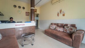 A reception area with a reception desk, a brown sofa, a cart, and a wall clock. - Hotel Kailash Park (Mumbai)
