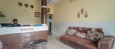 A reception area with a reception desk, a brown sofa, a cart, and a wall clock.