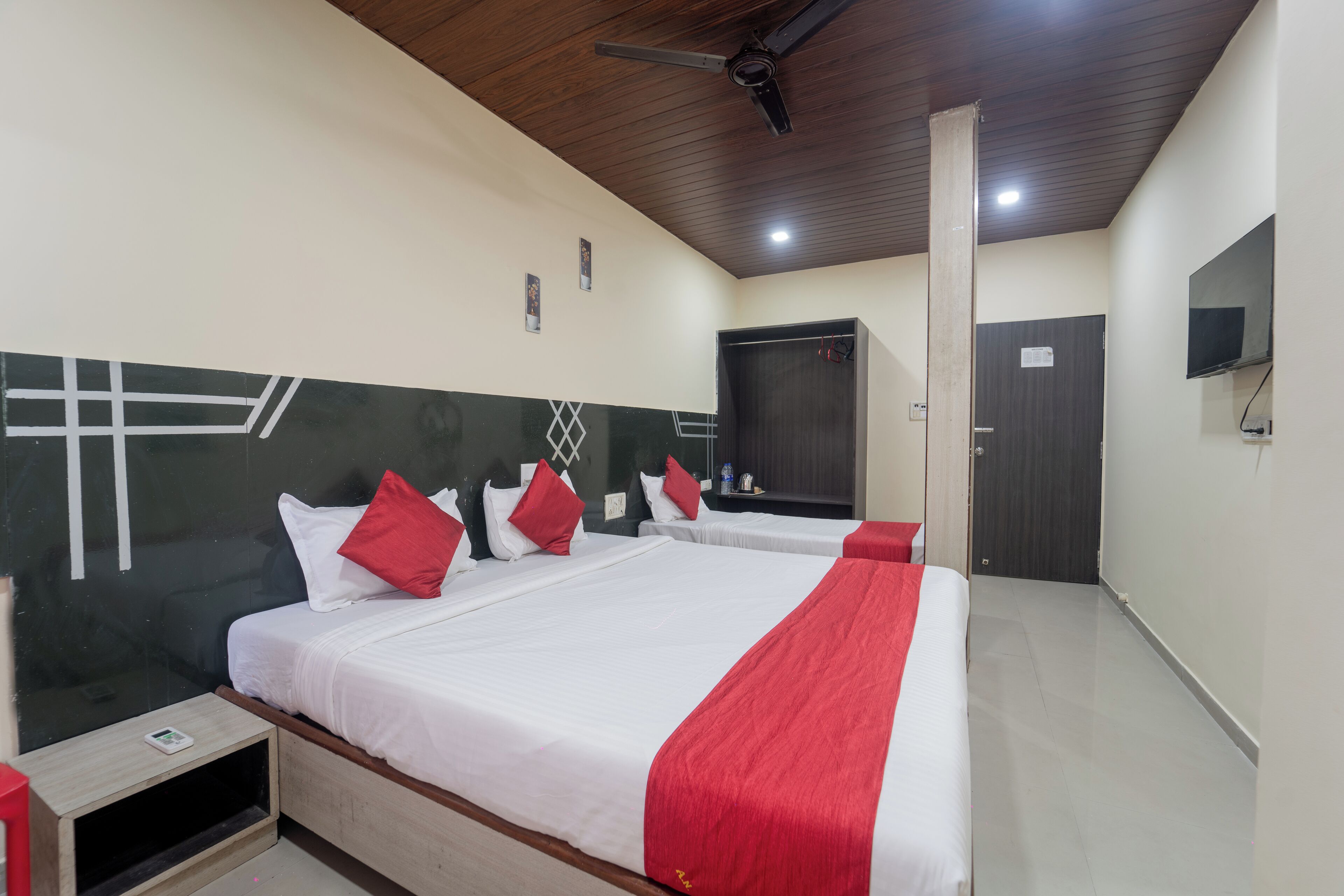 Habitación de hotel con dos camas, ventilador de techo, televisor y una puerta.