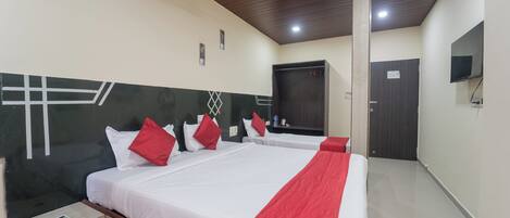 Habitación de hotel con dos camas, ventilador de techo, televisor y una puerta.