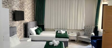 A hotel room with two beds, a television, a seating area with a chair and a small table, and a brick wall.