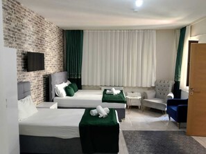 Une chambre d’hôtel avec deux lits, une télévision, un coin salon avec un fauteuil et une petite table, et un mur en briques.