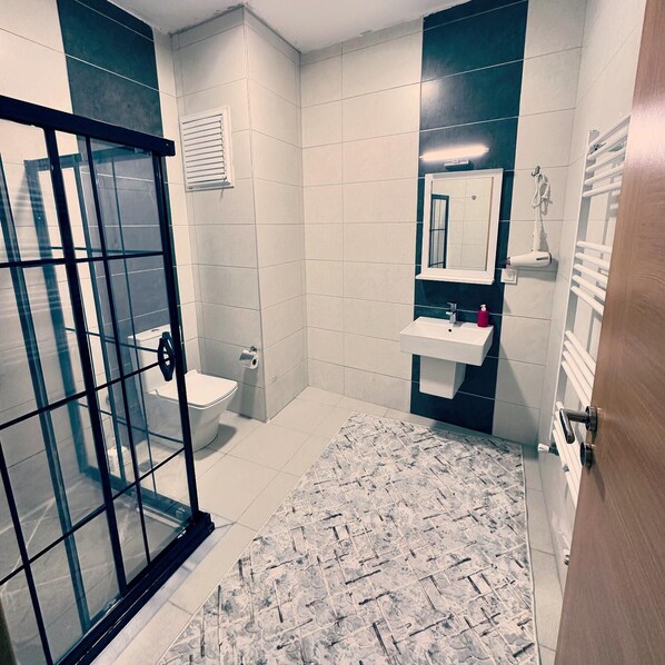 Une salle de bain avec une douche à parois de verre, des toilettes, un lavabo avec un miroir et un porte-serviettes.