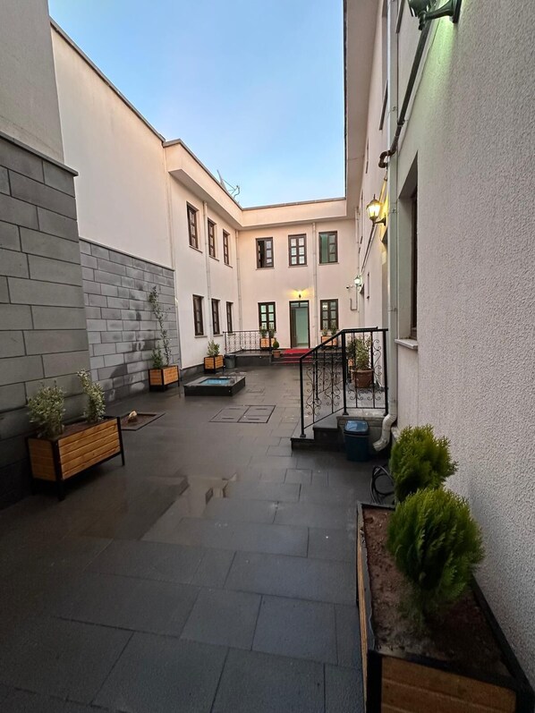 A courtyard with a central staircase, potted plants, and a building with multiple windows.