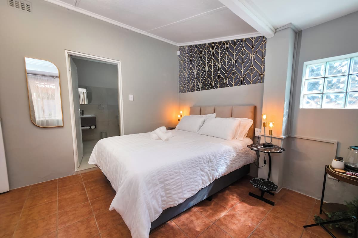A neatly made bed with white linens, a bedside table with a lamp, and a patterned wall above the bed.