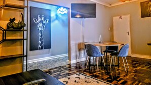 Une chambre d’hôtel moderne dotée d’une grande fresque murale, d’un téléviseur à écran plat, d’une table à manger avec des chaises et d’un sol à motifs.