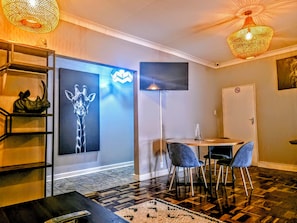 Una moderna camera d'albergo con un grande murale, una TV a schermo piatto, un tavolo da pranzo con sedie e un pavimento decorato.