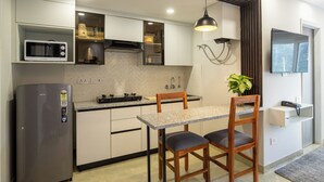 A compact kitchen with a built-in microwave, a stove, and a sink. There is a dining table with two chairs and a potted plant on the counter. - Bedchambers Apart hotel Sec 39 (Gurugram)