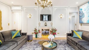 Ein geräumiges Wohnzimmer mit zwei Sofas, einer Chandelüster, einem Kamin und einem Flachbildfernseher.