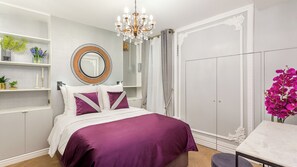 Ein Schlafzimmer mit Bett, Kleiderschrank, Schminktisch mit Spiegel und einer Chandelier.
