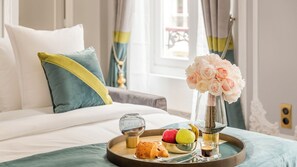 Ein schön gedecktes Frühstücksbrettchen auf einem Bett, dazu eine Blumenvase, ein Croissant, ein Apfel, eine Birne und eine Kaffeetasse.