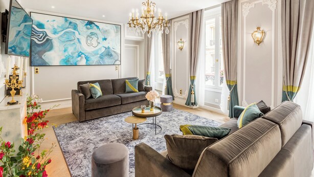 Ein geräumiges Wohnzimmer mit einer grauen Sofagarnitur, einem runden Couchtisch und einem großen abstrakten Gemälde an der Wand.