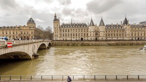 Ein historisches Gebäude mit einem großen zentralen Turm und mehreren kleineren Türmen, einer Brücke mit Bögen und einem Fluss im Vordergrund.
