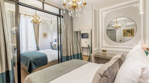 Ein Hotelzimmer mit einem großen Bett, einem separaten Schlafbereich mit Vorhängen, einem Schminktisch mit Spiegel und einer Kristallleuchtre.
