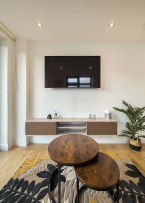 A modern living room with a flat-screen TV mounted on the wall, a wooden coffee table, and a patterned rug. - Spacious 2BR, 2 Bath with Balcony Sleeps 6 (Greater London)