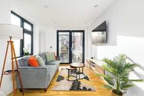 A modern living room with a grey sofa, a floor lamp, a coffee table, and a large window with a view of a cityscape.