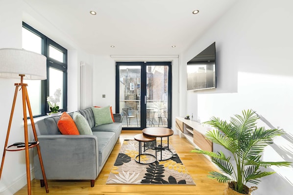 A modern living room with a grey sofa, a floor lamp, a coffee table, and a large window with a view of a cityscape.
