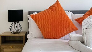 A hotel room with a bed, pillows, a nightstand, a lamp, and two framed artworks on the wall. - Spacious 2BR, 2 Bath with Balcony Sleeps 6 (Greater London)