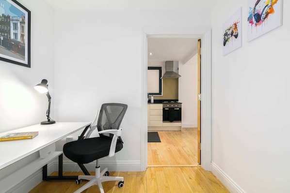 A modern, minimalistic room with a desk, chair, and a view into the kitchen.