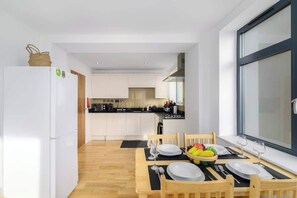 A modern kitchen with white cabinets, a dining area with a wooden table set for two, and a large window.