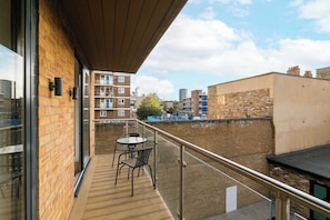 A balcony with a glass door, a small table with chairs, and a view of surrounding buildings.