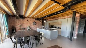 A spacious kitchen with a central island, exposed wooden beams, and a brick wall.