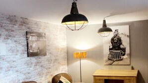 Un salon chaleureux avec un mur en briques, un canapé en cuir marron, un bureau en bois et une valise ancienne.
