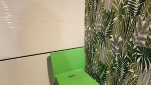 Une chaise verte, placée dans un coin, avec un sol carrelé de carreaux blancs et un mur orné d’un motif de feuilles.
