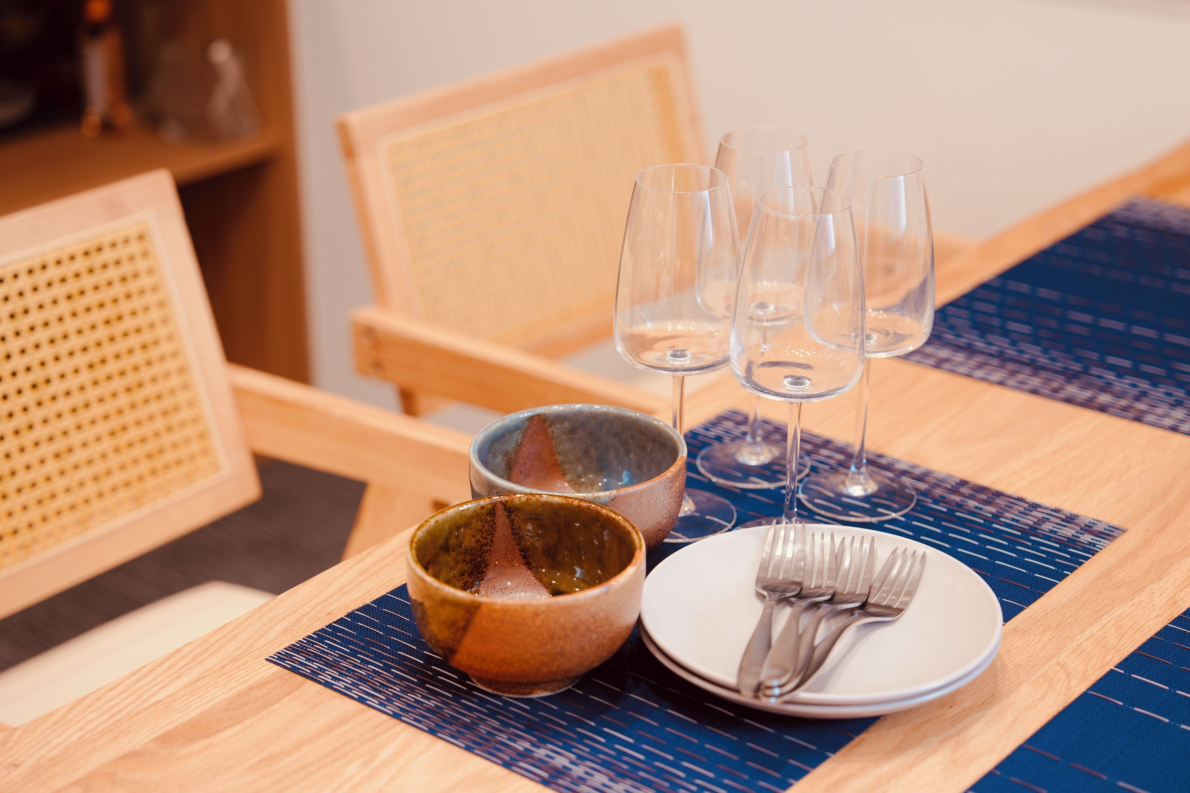 Una mesa de comedor con un posavasos, un plato con cubiertos y tres copas de vino.