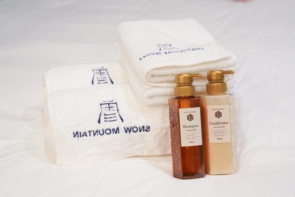 A set of toiletries including a shampoo bottle, conditioner, and two towels with a logo.