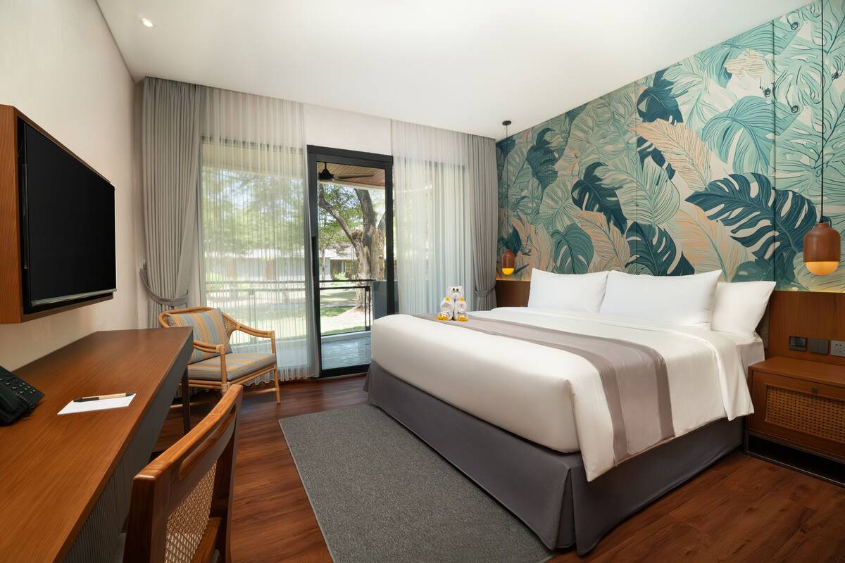 A hotel room with a bed, a desk, a chair, a TV, and a large window with curtains.