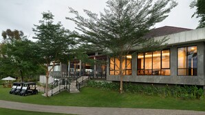 A modern building with a staircase leading to a balcony, surrounded by lush greenery and a well-maintained lawn. - House Sira Lombok (Tanjung)