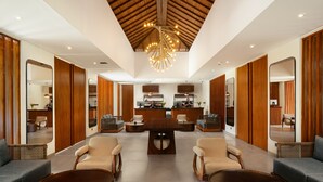 A spacious lobby with a central reception desk, seating area, and a high ceiling with a unique chandelier. - House Sira Lombok (Tanjung)