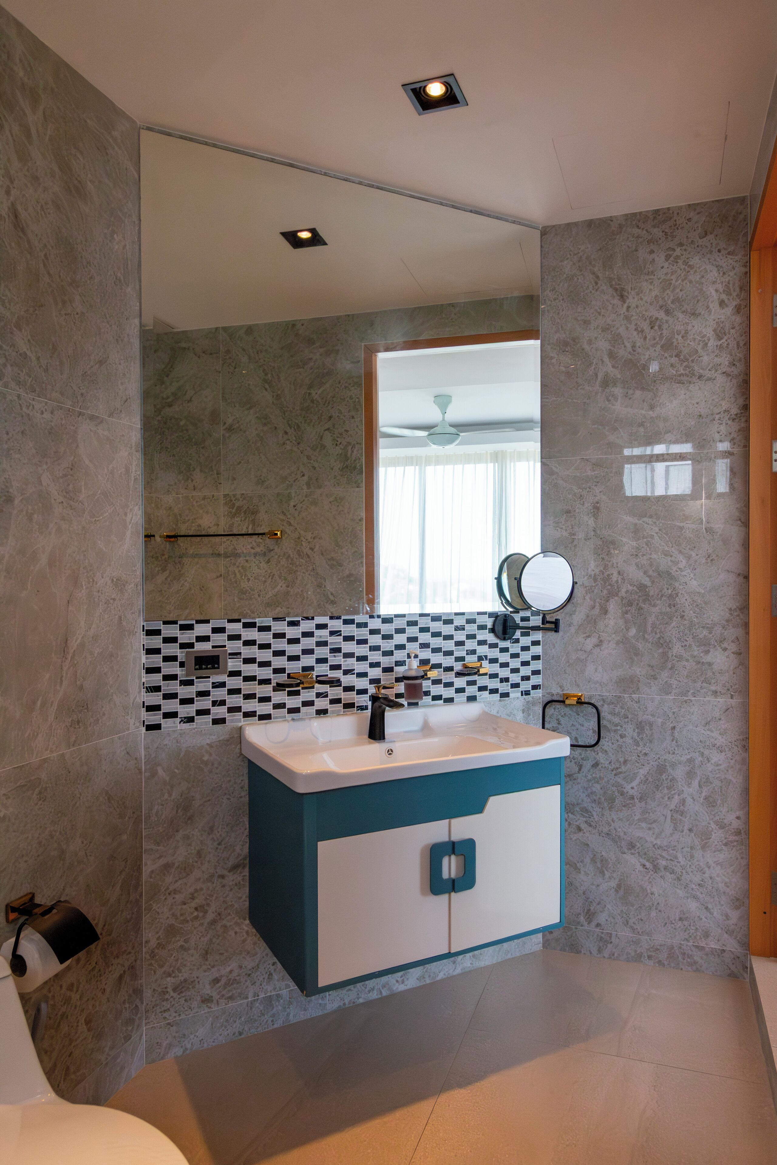A modern bathroom with a marble wall, a white and blue vanity, a mirror, and a ceiling light.