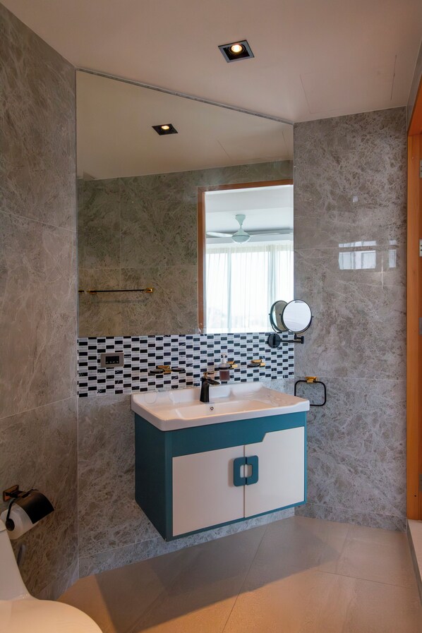 A modern bathroom with a marble wall, a white and blue vanity, a mirror, and a ceiling light. - Seaview Hillside 3BR Infinity Pool V254 (Koh Samui)