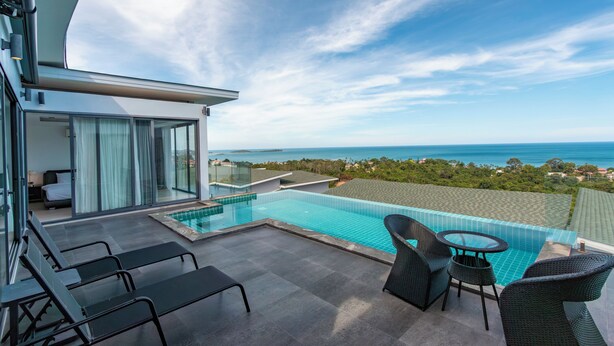 A modern hotel balcony with a pool, seating area, and a view of the ocean.