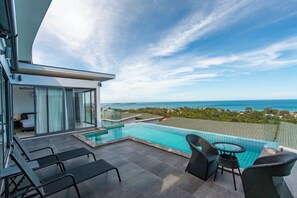 A modern hotel balcony with a pool, seating area, and a view of the ocean. - Seaview Hillside 3BR Infinity Pool V254 (Koh Samui)