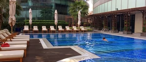 A swimming pool with lounge chairs and umbrellas, surrounded by modern buildings.