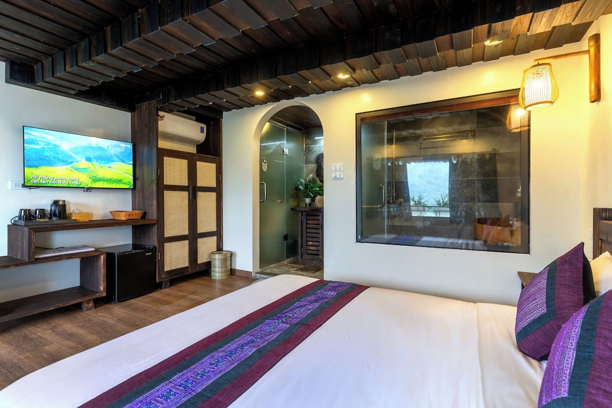 Een hotelkamer met een groot bed, een televisie aan de muur, een houten plafond en een raam met uitzicht.