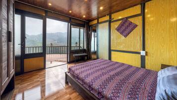 A bedroom with a large bed, wooden flooring, a balcony with a view, and a wooden ceiling.