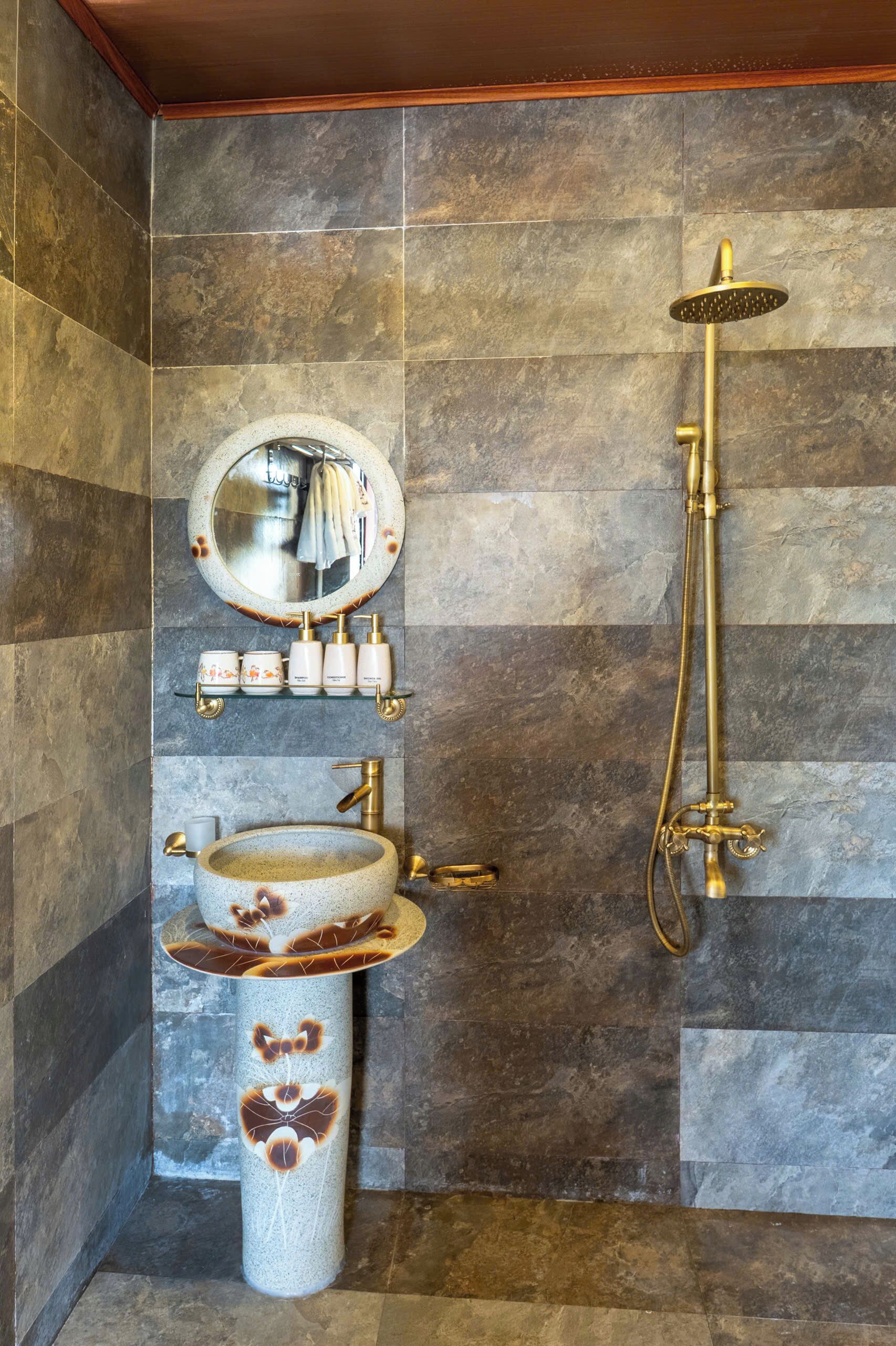 A bathroom with a stone sink, a round mirror, and a gold showerhead.