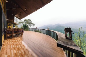 Eine Holzterrasse mit geschwungener Geländer, einem Tisch mit Stühlen und Blick auf Berge.
