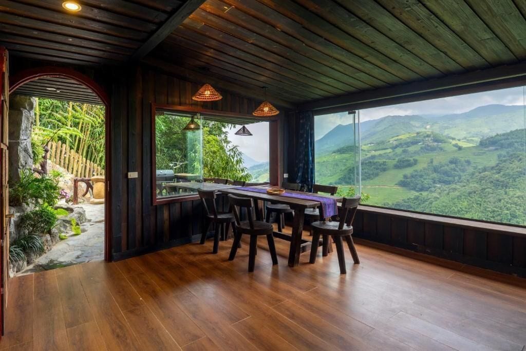 Un coin repas avec une table et des chaises en bois, de grandes fenêtres offrant une vue sur des collines verdoyantes.
