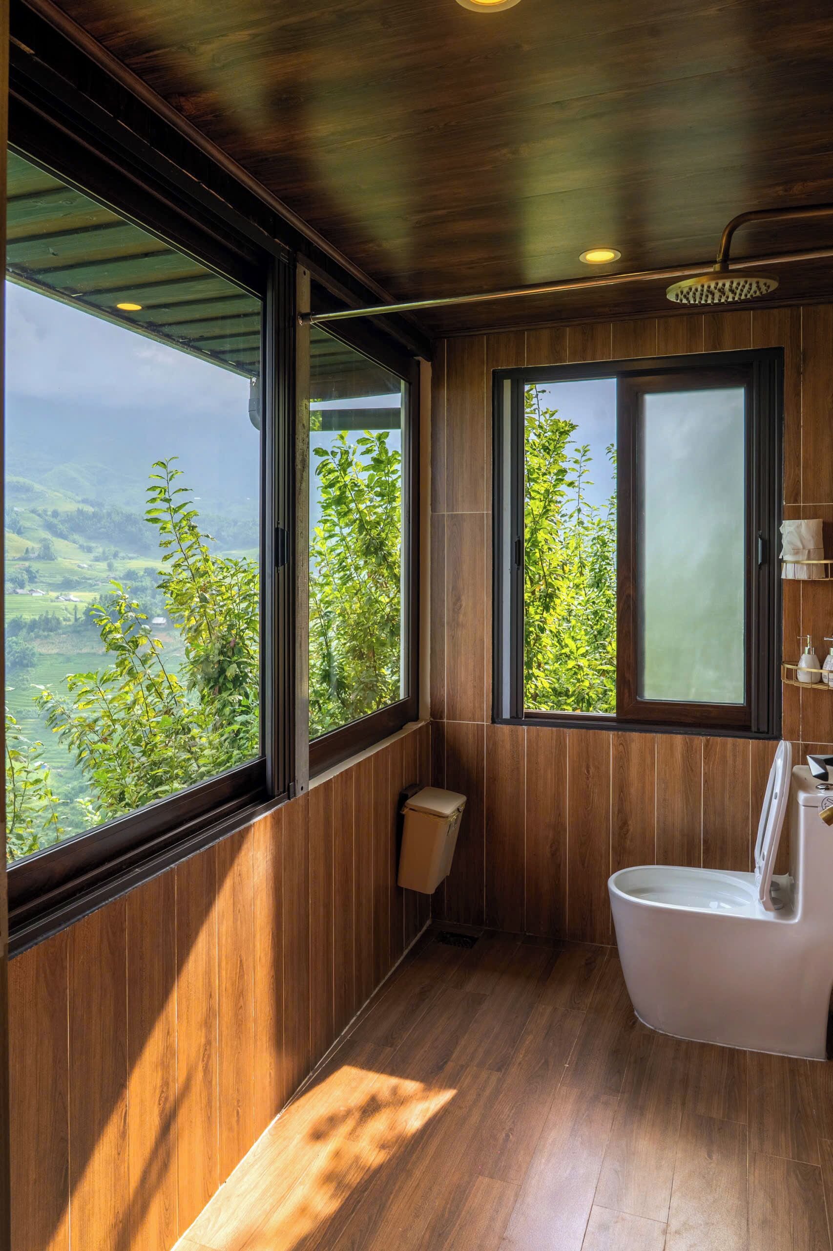 Ein Badezimmer mit Holzwänden, einer Toilette und einem Fenster mit Blick ins Grüne.