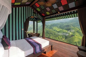 Ein Schlafzimmer mit einem großen Bett, Holzboden und Blick auf grüne Hügel.