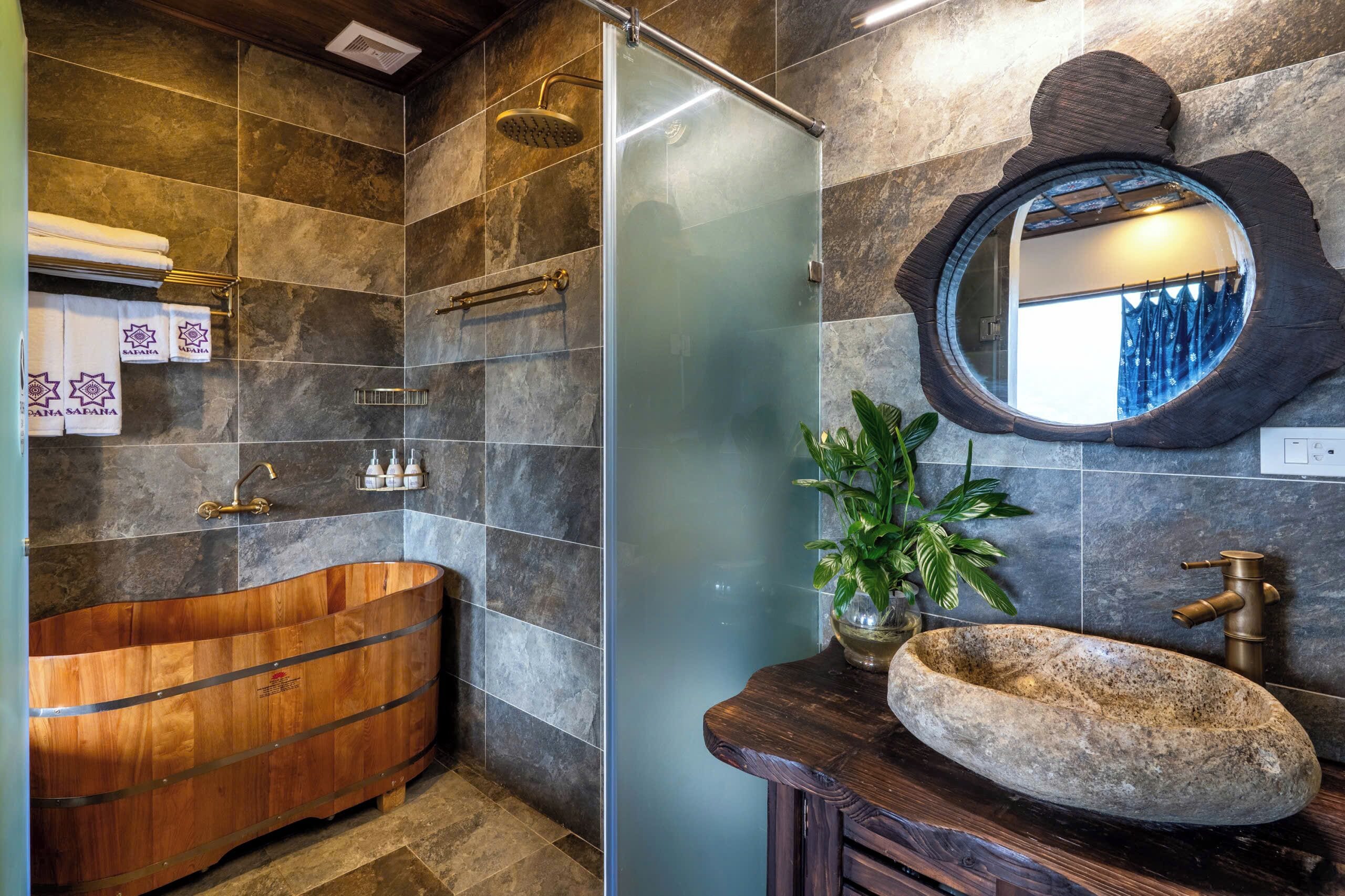 A bathroom with a wooden bathtub, a stone sink, and a large mirror.