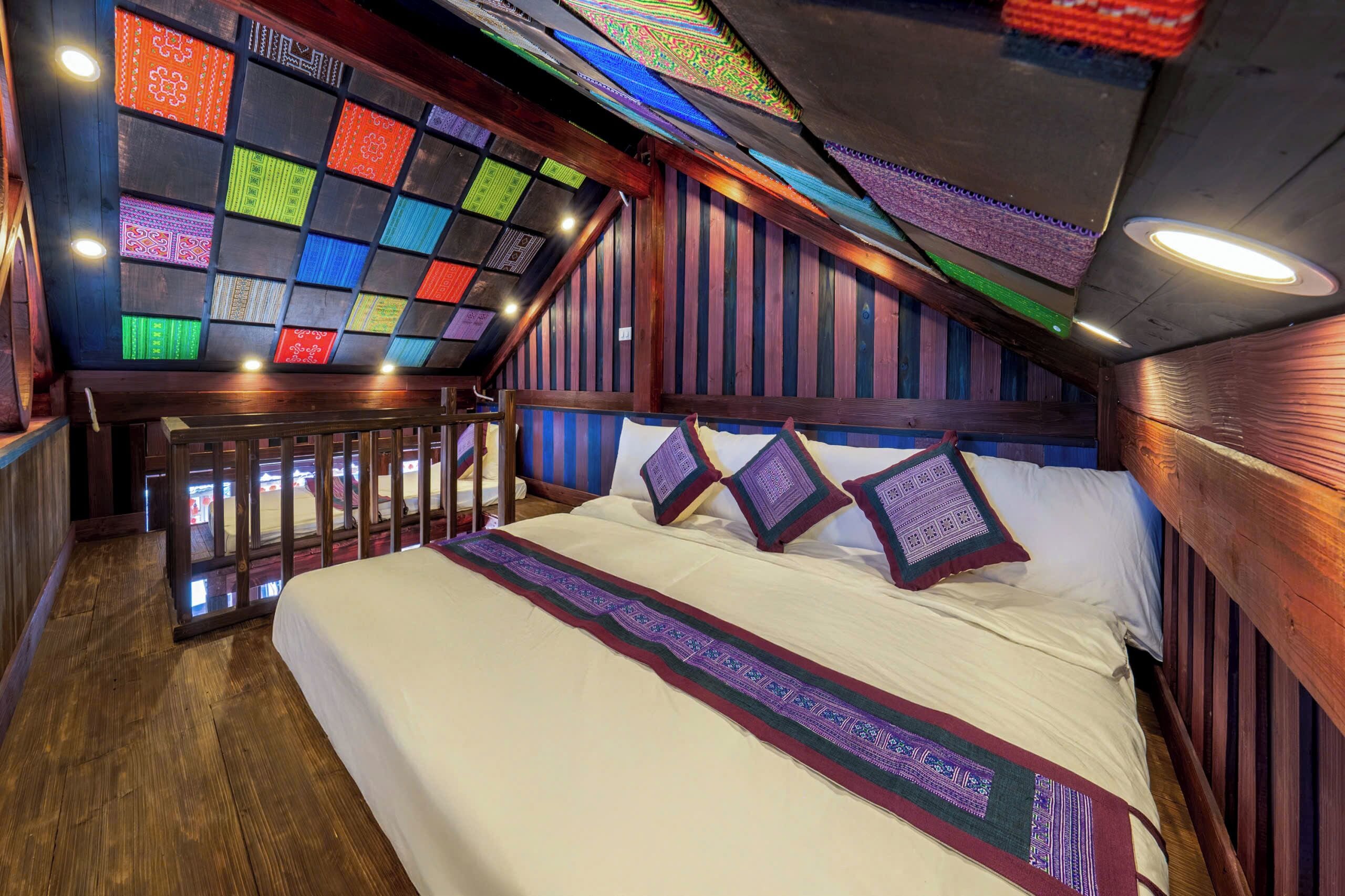Quarto com uma cama grande, cabeceira de madeira e vista para o exterior através de uma janela com padrões coloridos.